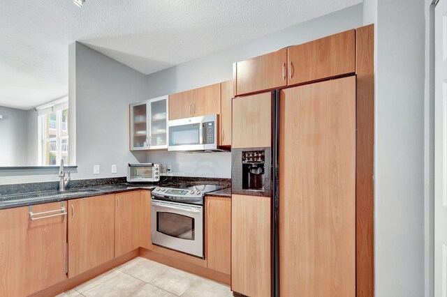 kitchen featuring sink, dark stone countertops, a textured ceiling, light tile patterned flooring, and stainless steel appliances