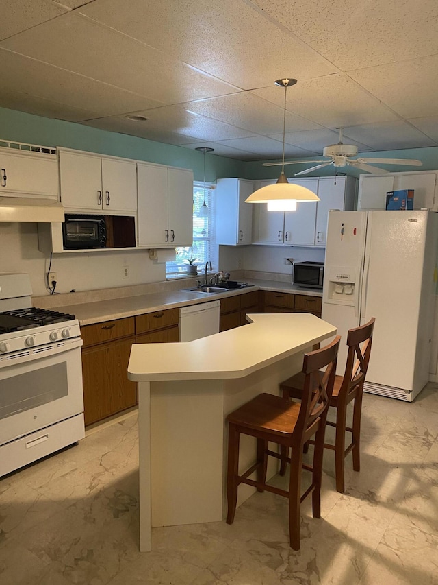 kitchen featuring white appliances, a breakfast bar, decorative light fixtures, light countertops, and a paneled ceiling