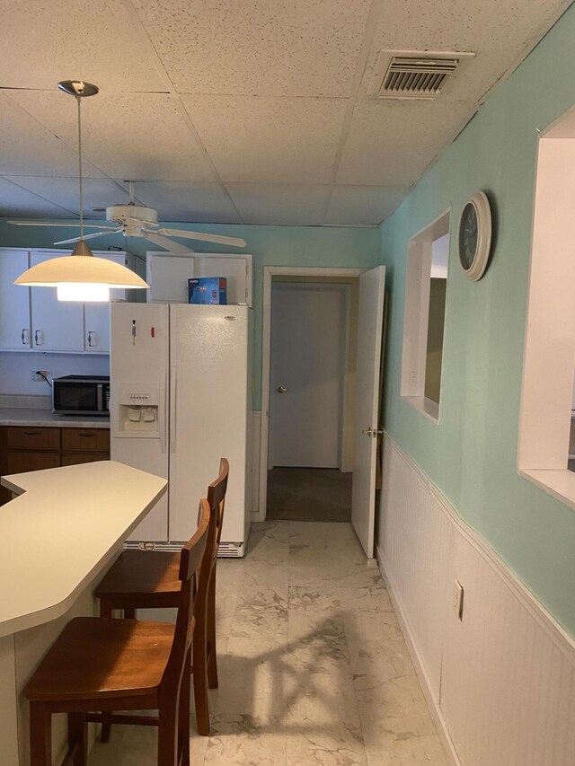 kitchen with a drop ceiling, a wainscoted wall, visible vents, marble finish floor, and white fridge with ice dispenser