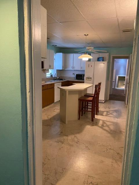 kitchen featuring a paneled ceiling, white appliances, visible vents, light countertops, and a center island