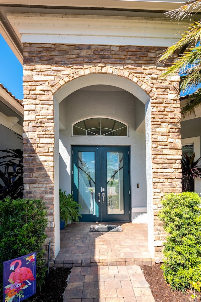 view of exterior entry with stone siding, french doors, and stucco siding