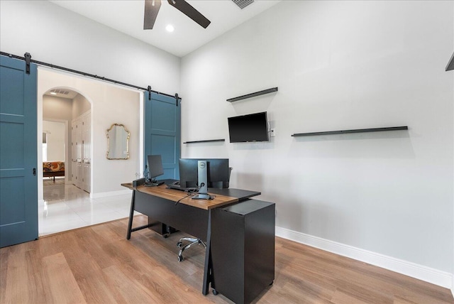 office space with arched walkways, a barn door, a ceiling fan, baseboards, and light wood finished floors