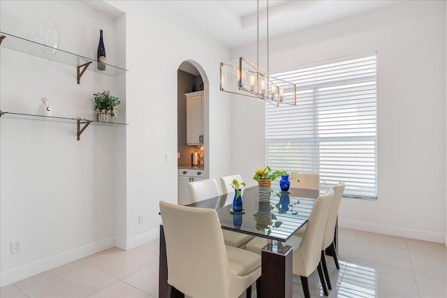 dining space featuring light tile patterned floors, baseboards, arched walkways, and a chandelier