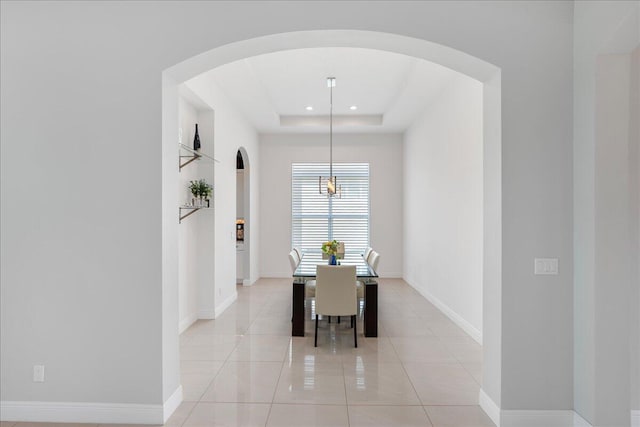 dining space featuring light tile patterned floors, baseboards, arched walkways, a tray ceiling, and recessed lighting