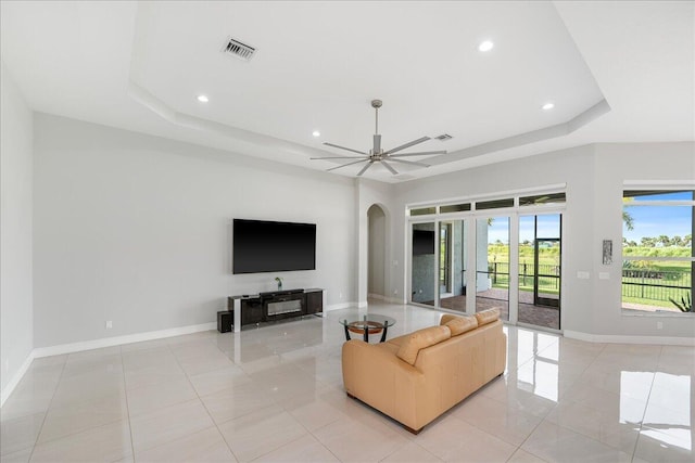 living area with a ceiling fan, arched walkways, a raised ceiling, and baseboards