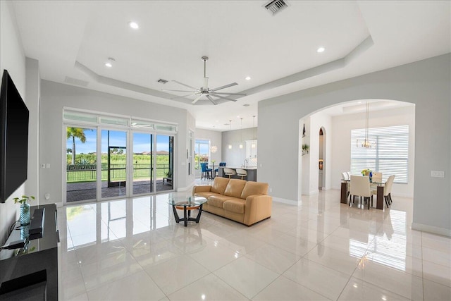 living room with baseboards, visible vents, a raised ceiling, and arched walkways