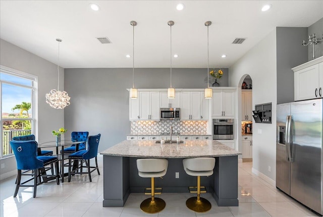 kitchen featuring visible vents, decorative backsplash, an island with sink, light stone counters, and stainless steel appliances