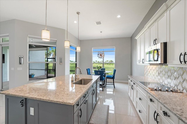 kitchen with black electric stovetop, stainless steel microwave, decorative backsplash, a sink, and an island with sink