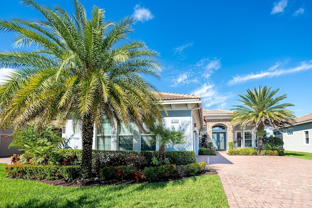 mediterranean / spanish-style house featuring a tile roof, french doors, decorative driveway, and stucco siding