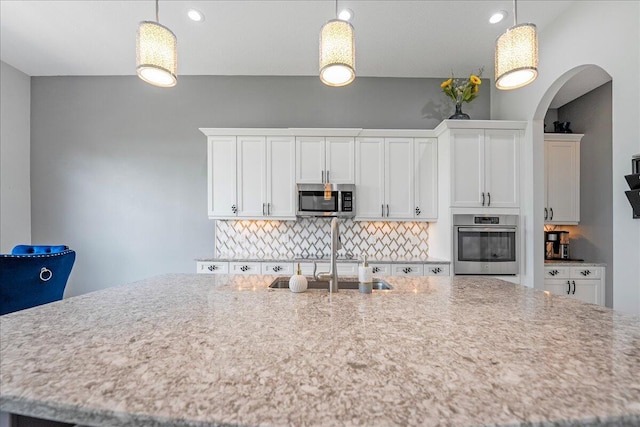 kitchen featuring pendant lighting, tasteful backsplash, appliances with stainless steel finishes, white cabinetry, and a sink