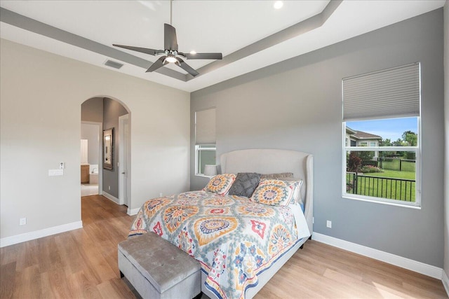 bedroom featuring a tray ceiling, visible vents, baseboards, and wood finished floors