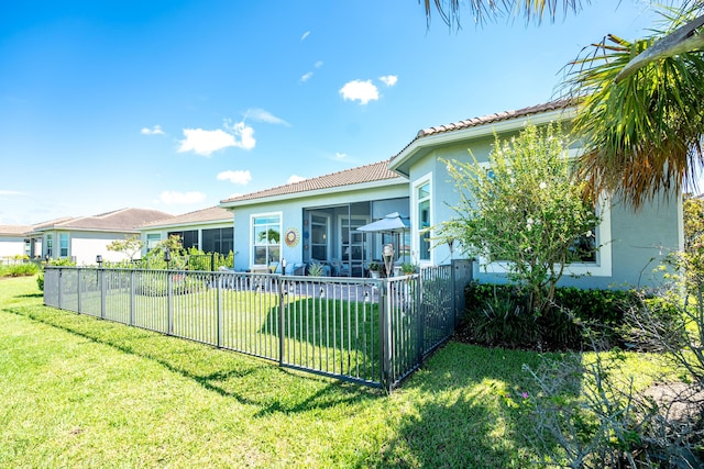 rear view of property with a sunroom, a tiled roof, fence, a yard, and stucco siding