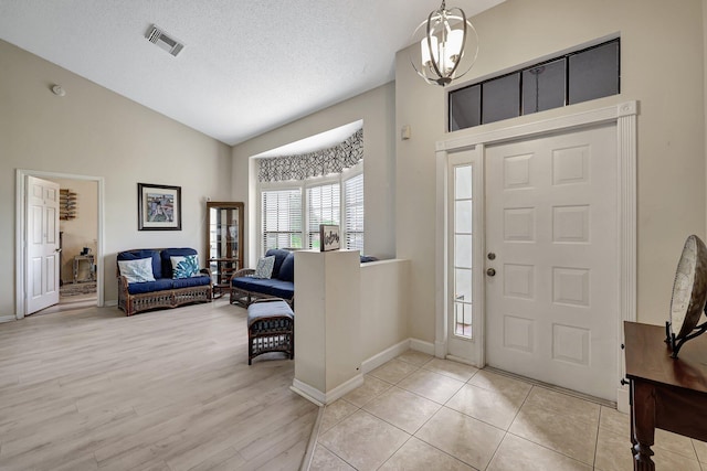 foyer with light hardwood / wood-style flooring, lofted ceiling, a textured ceiling, and an inviting chandelier