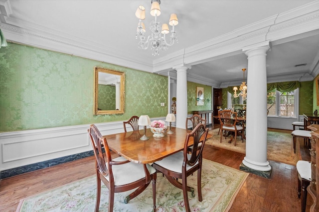 dining area with a wainscoted wall, crown molding, wood finished floors, a chandelier, and ornate columns