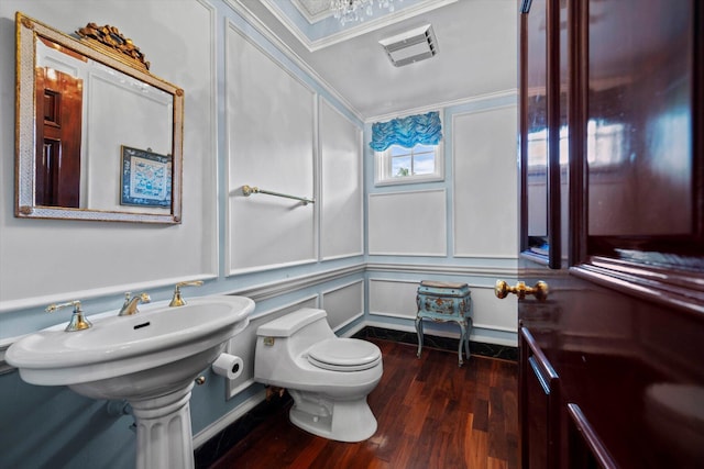 half bathroom featuring toilet, a decorative wall, wood finished floors, visible vents, and crown molding