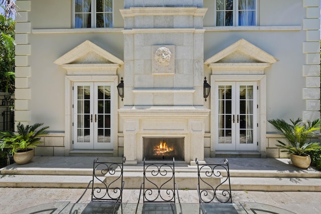 view of exterior entry featuring a lit fireplace, french doors, and stone siding