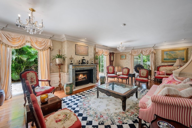 living room featuring an inviting chandelier, ornamental molding, a fireplace with flush hearth, wainscoting, and wood finished floors