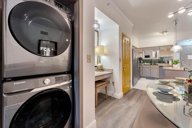 laundry room with light wood finished floors, laundry area, stacked washer and clothes dryer, ornamental molding, and a sink