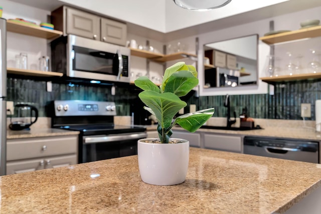 kitchen featuring open shelves, appliances with stainless steel finishes, a sink, and light stone countertops