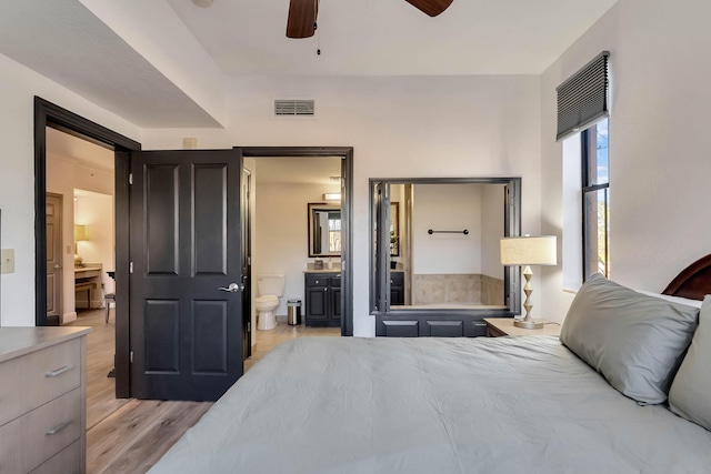 bedroom featuring light wood-type flooring, ensuite bath, visible vents, and a ceiling fan