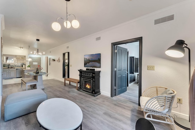 living room featuring light wood-type flooring, an inviting chandelier, visible vents, and ornamental molding