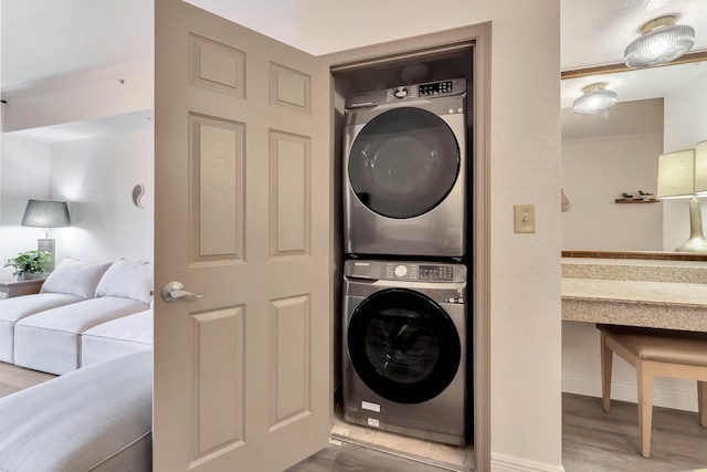 clothes washing area featuring laundry area, ornamental molding, wood finished floors, and stacked washer and clothes dryer