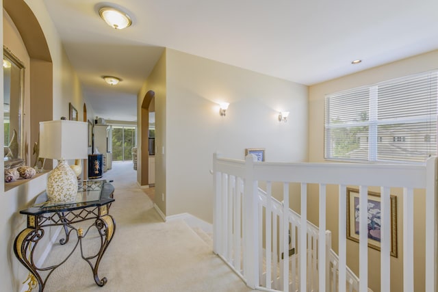 corridor with arched walkways, baseboards, light carpet, and an upstairs landing