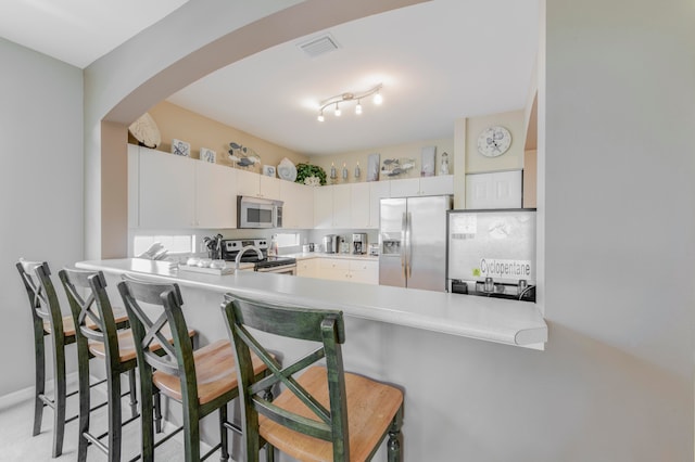 kitchen featuring a kitchen breakfast bar, track lighting, white cabinetry, stainless steel appliances, and kitchen peninsula