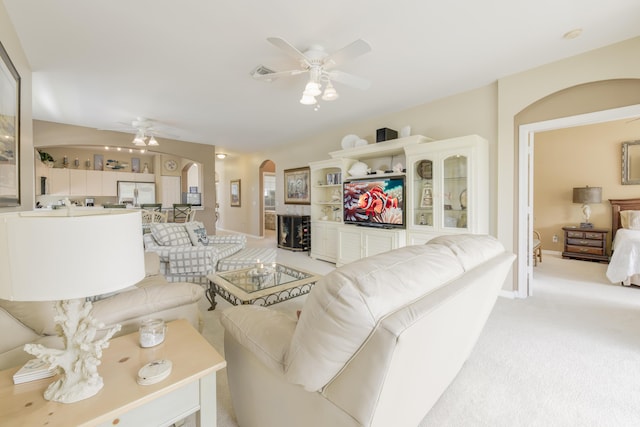 living area with arched walkways, visible vents, light carpet, ceiling fan, and baseboards