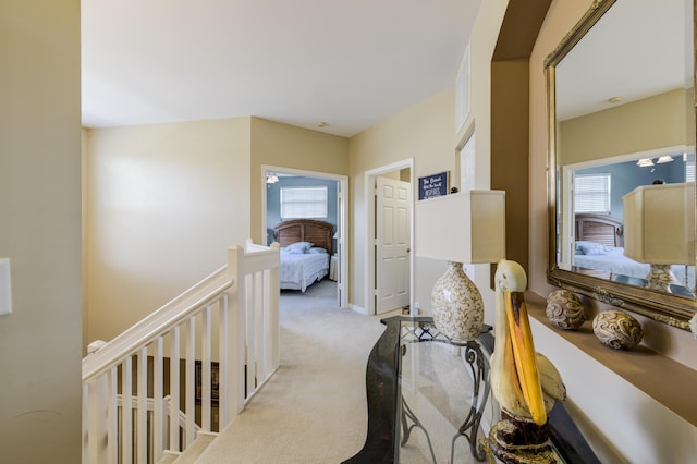 corridor with a healthy amount of sunlight, light carpet, and an upstairs landing