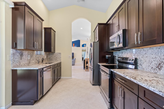 kitchen featuring stainless steel appliances, light stone countertops, vaulted ceiling, and dark brown cabinets