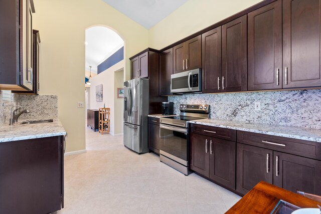 kitchen featuring light stone counters, dark brown cabinetry, appliances with stainless steel finishes, and sink