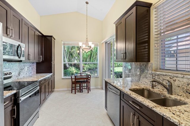 kitchen featuring pendant lighting, lofted ceiling, sink, stainless steel appliances, and light stone countertops