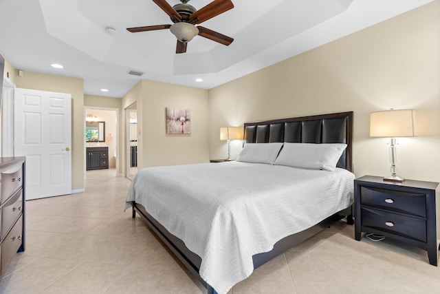 bedroom with light tile patterned flooring, ensuite bathroom, ceiling fan, and a tray ceiling