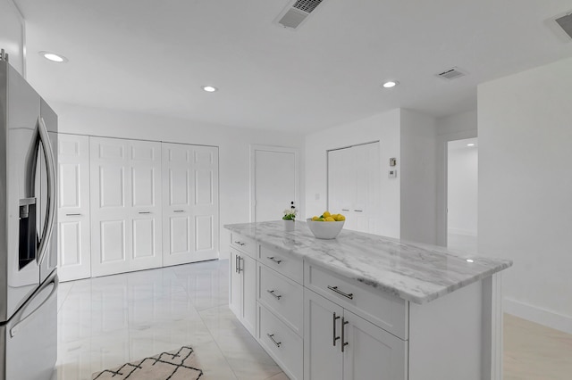 kitchen featuring stainless steel fridge, light tile flooring, light stone counters, a center island, and white cabinetry