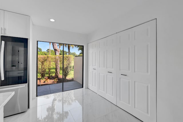 unfurnished bedroom featuring fridge, a closet, light tile flooring, and access to exterior