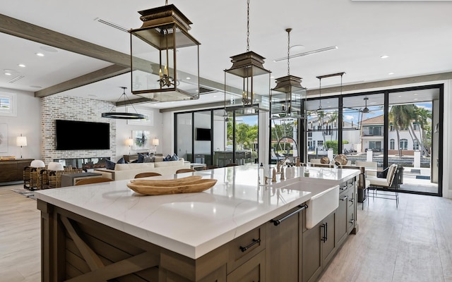 kitchen with decorative light fixtures, light hardwood / wood-style flooring, sink, and an island with sink