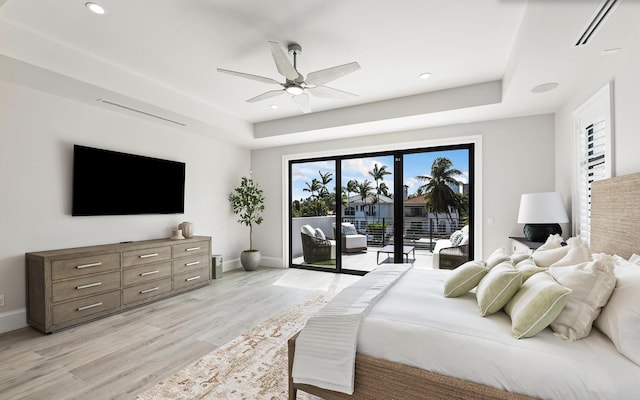 bedroom featuring access to outside, ceiling fan, light hardwood / wood-style floors, and a tray ceiling