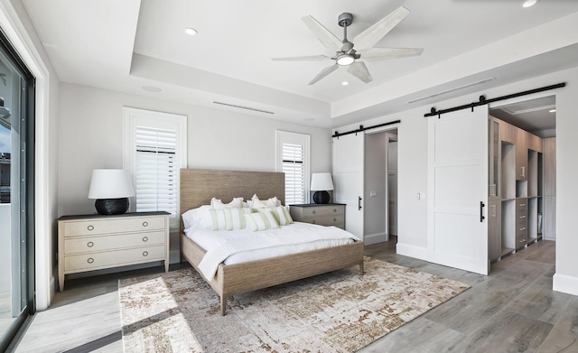 bedroom with ceiling fan, a barn door, a raised ceiling, and wood-type flooring