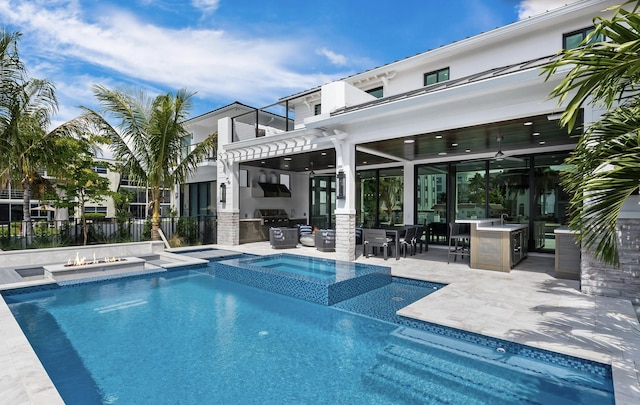 view of swimming pool with ceiling fan, an in ground hot tub, a grill, a patio area, and exterior kitchen