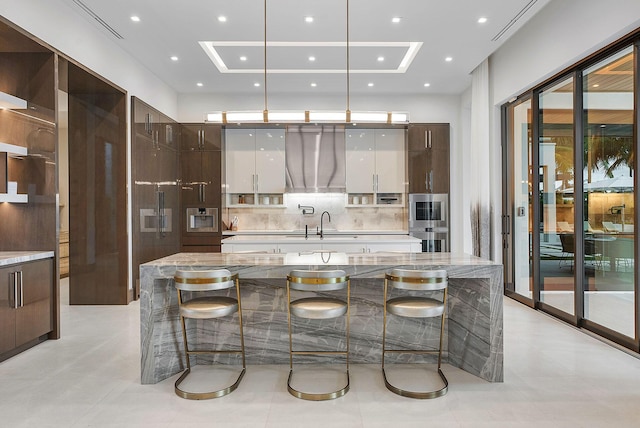 kitchen featuring exhaust hood, light stone countertops, modern cabinets, a kitchen bar, and a large island with sink