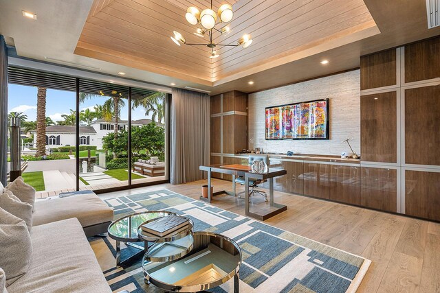 living room with a chandelier, a towering ceiling, light hardwood / wood-style floors, and a raised ceiling