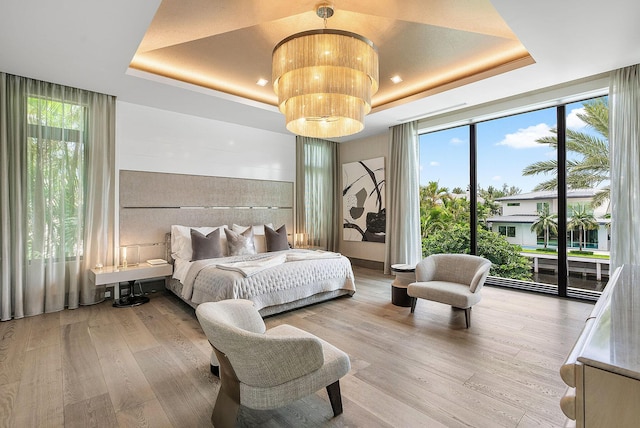 bedroom with light wood finished floors, access to outside, floor to ceiling windows, and a raised ceiling