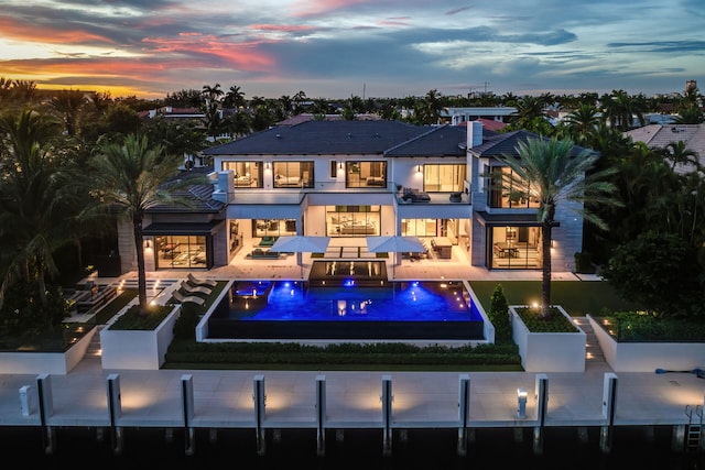 back house at dusk with a swimming pool with hot tub, a balcony, and a patio area