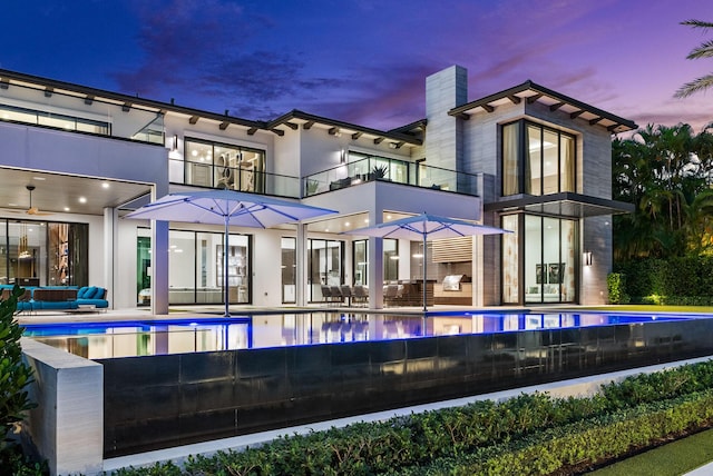 back house at dusk with an outdoor living space, ceiling fan, a balcony, and a patio