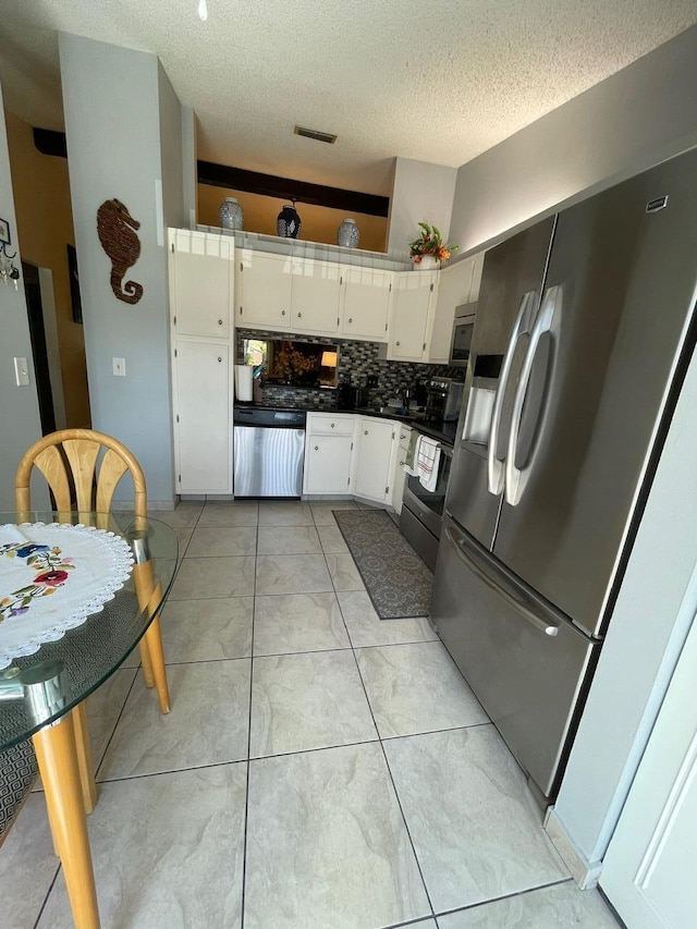 kitchen featuring stainless steel appliances, white cabinets, decorative backsplash, a textured ceiling, and light tile patterned floors