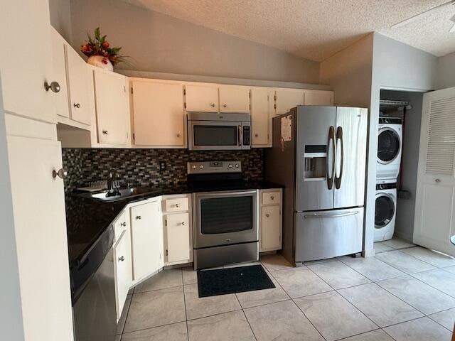 kitchen featuring lofted ceiling, white cabinetry, stacked washer / drying machine, and appliances with stainless steel finishes