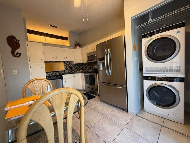 kitchen featuring stainless steel appliances, light tile patterned flooring, stacked washer and clothes dryer, backsplash, and white cabinets