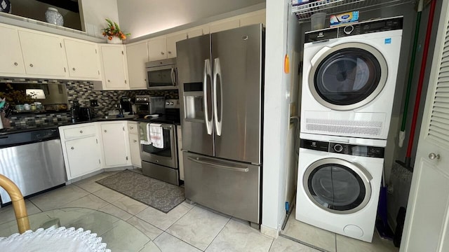 kitchen featuring stacked washing maching and dryer, white cabinetry, appliances with stainless steel finishes, light tile patterned floors, and decorative backsplash