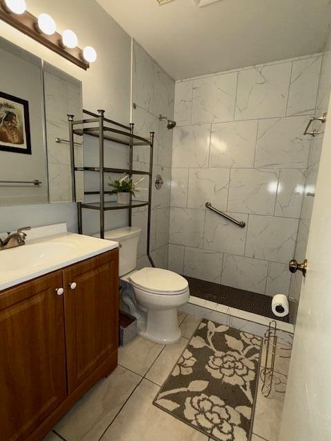 bathroom featuring tile patterned flooring, tiled shower, toilet, and vanity